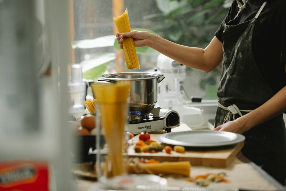 Crop anonymous female chef in apron putting spaghetti into pan with boiling water while cooking pasta in modern kitchen