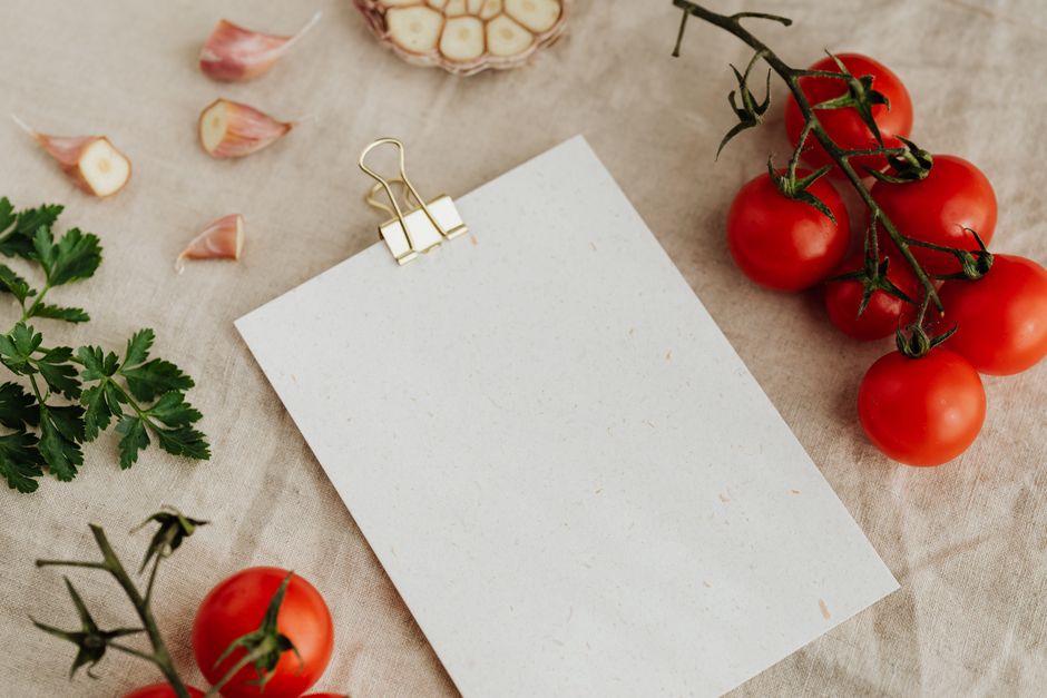A rustic kitchen scene with tomatoes, garlic, parsley, and blank paper on linen.