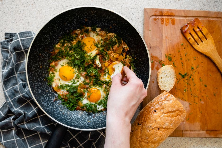 Top view of shakshouka in a frying pan with bread on a wooden chopping board.