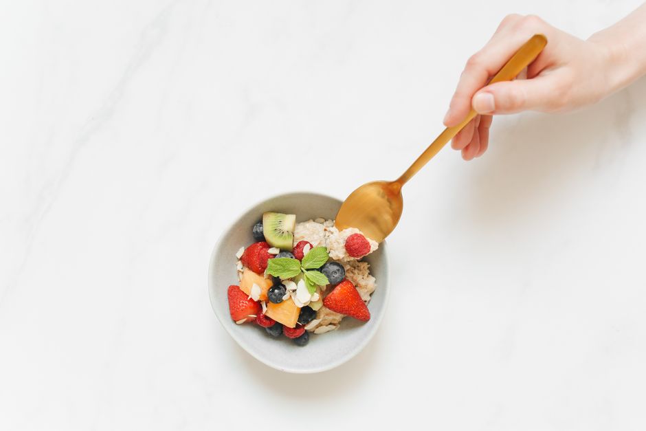 Top view of a colorful fruit and oatmeal breakfast bowl with a hand holding a spoon.